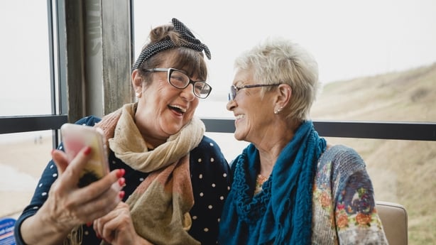 two senior women laughing while looking at a phone