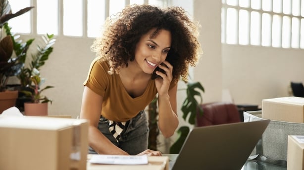 Young female talking on smart phone while using laptop. Confident businesswoman is working at home office. She is having curly hair.