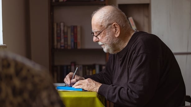 An older man writing in a journal.